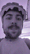 a selfie of a white person, wearing either headphones or a helmet, making an odd expression. the photo is edited to be colorized into a monochrome purple-ish color palette.